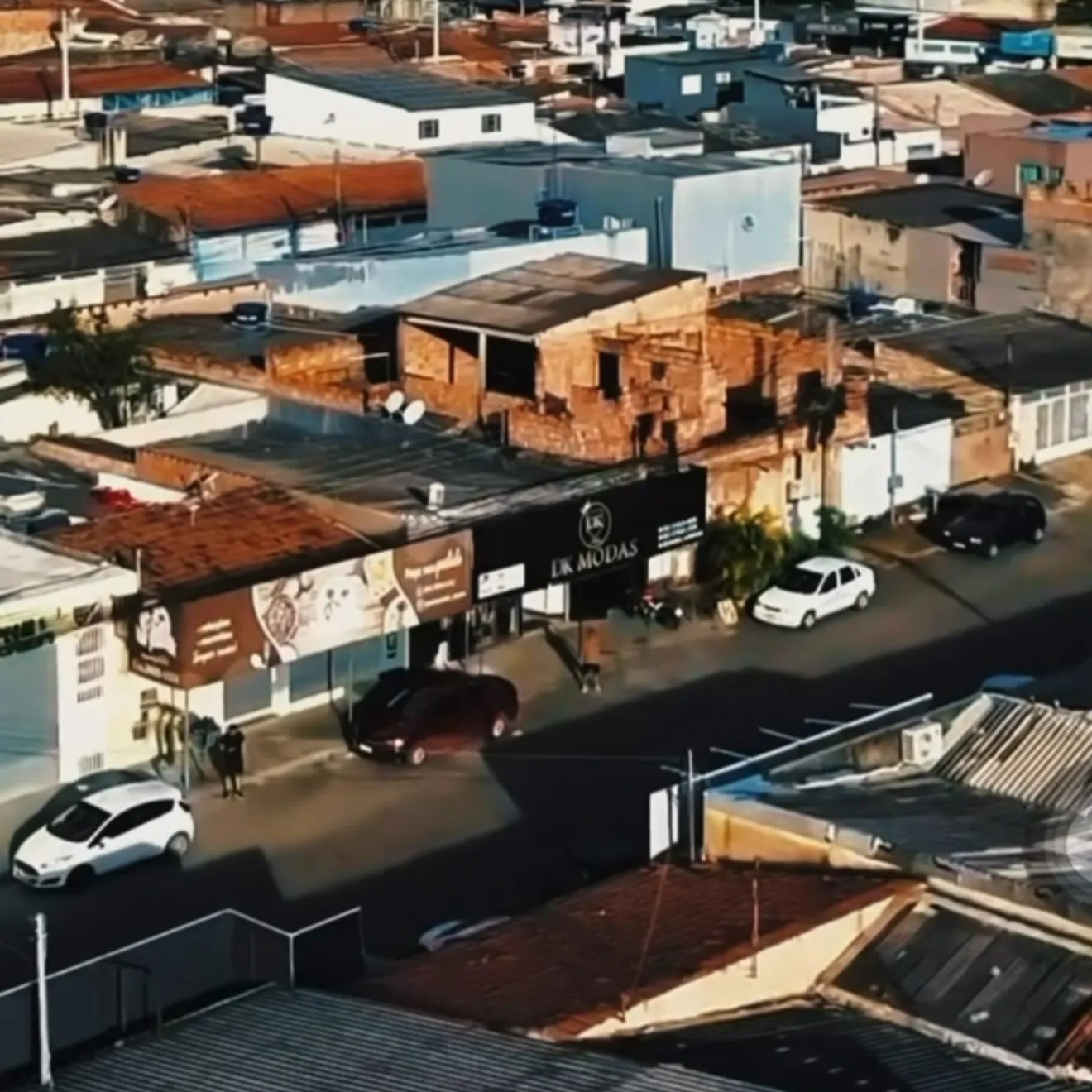 Cidade Ocidental vista de cima, no fim da tarde: telhados, uma rua com carros e, no meio dela, a fachada preta da DK Modas com o nome em dourado